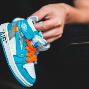 Vibrant blue and orange baby sneaker held in a hand, showcasing modern and trendy design.